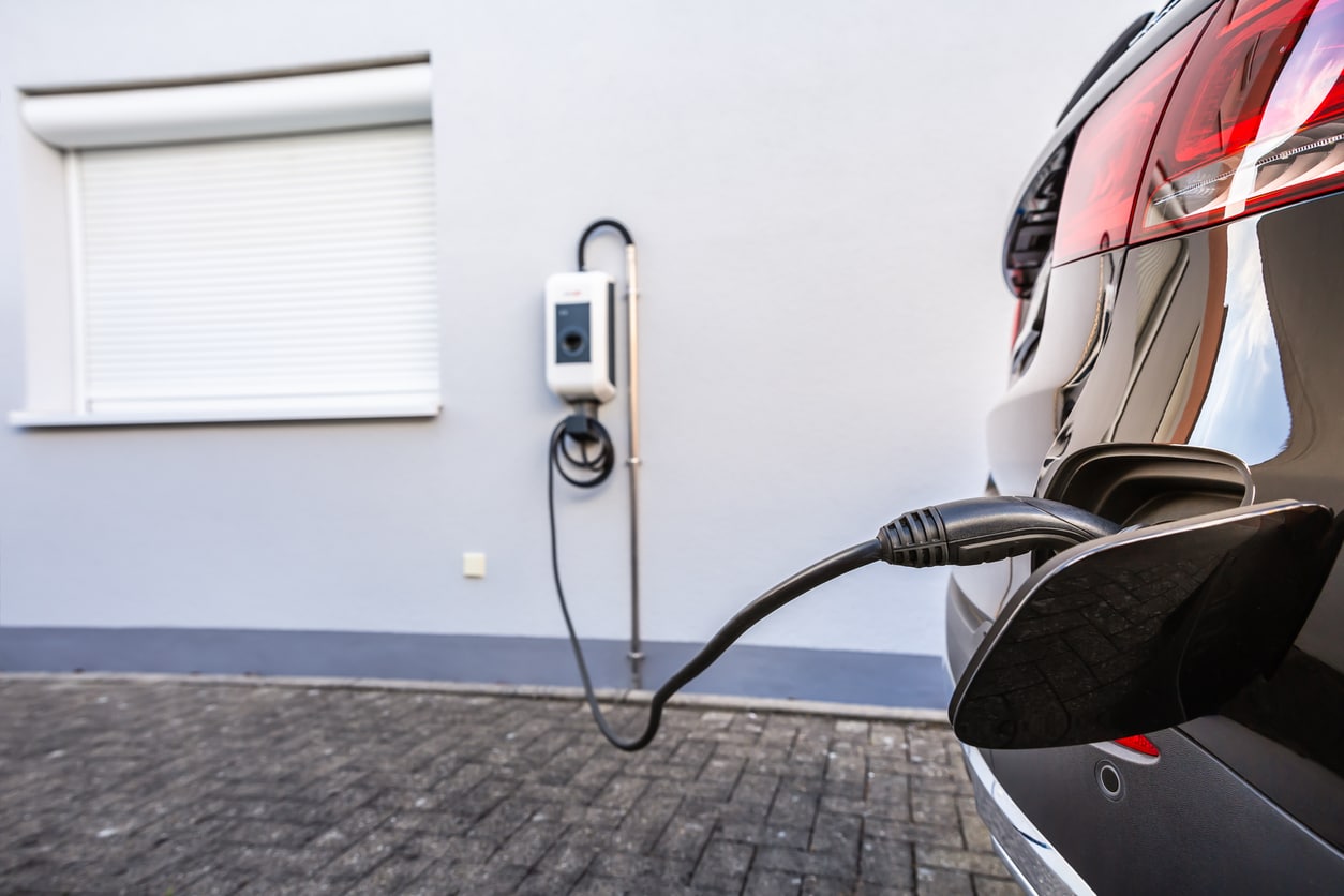 An electric vehicle charges in the driveway of a residential neighborhood using an EV charging station installed by Power Pros Electric.