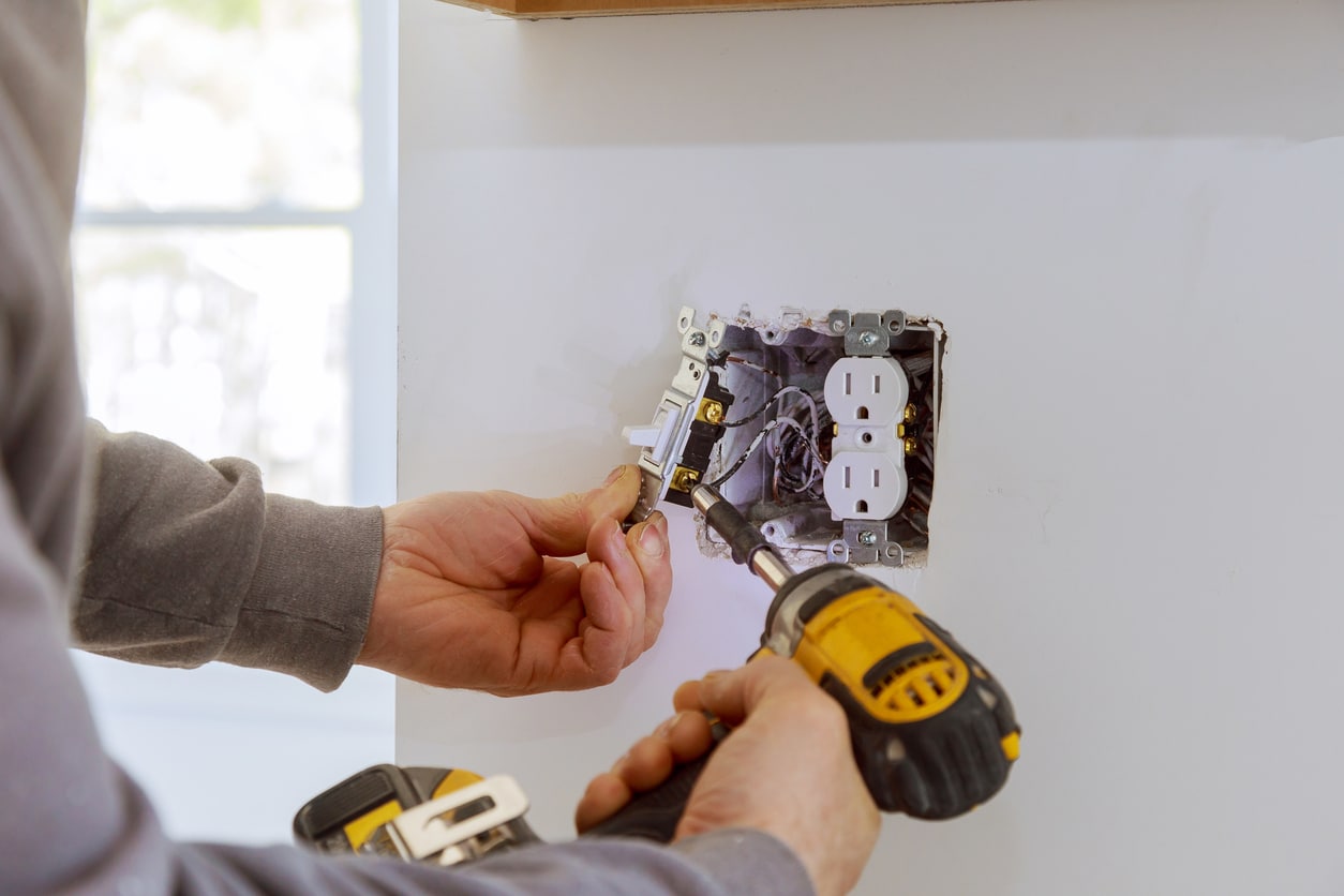 An electrician installs a wall outlet, illustrating safe, professional electrical work in a residential setting.